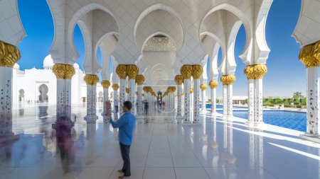 Foto de Sheikh Zayed Gran Mezquita timelapse hiperlapso en Abu Dhabi, la capital de los Emiratos Árabes Unidos. Gente caminando entre columnas. Cielo azul en el día soleado - Imagen libre de derechos