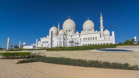 Téléchargez les photos : L'hyperlapsus intemporel de la Grande Mosquée Cheikh Zayed à Abu Dhabi, la capitale des Émirats arabes unis. Derrière avec des arbres. Ciel bleu au soleil - en image libre de droit