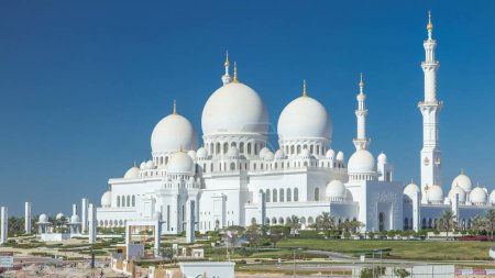 Photo for Sheikh Zayed Grand Mosque timelapse in Abu Dhabi, the capital city of United Arab Emirates. Back side with trees and traffic on the road from above. Blue sky at sunny day - Royalty Free Image