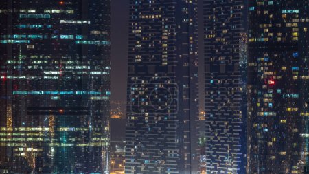 Foto de Ventanas de los rascacielos de varios pisos de iluminación de oficinas de vidrio y acero y personas dentro de timelapse. Luz intermitente en apartamentos. Abu Dhabi, Emiratos Árabes Unidos - Imagen libre de derechos
