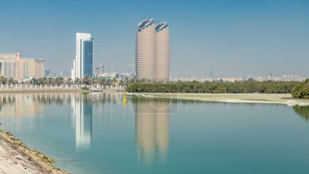 Foto de Vista del horizonte de los rascacielos con las torres Al Bahr en Abu Dhabi timelapse. Reflexiones sobre el agua y las palmas en la calle. Emiratos Árabes Unidos - Imagen libre de derechos