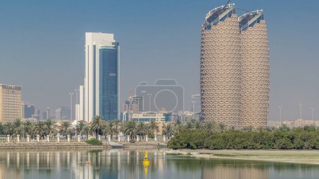 Téléchargez les photos : Vue des gratte-ciel skyline avec des tours Al Bahr à Abu Dhabi timelapse. Réflexions sur l'eau et les paumes dans la rue. Émirats arabes unis - en image libre de droit