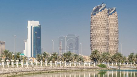 Photo for View of skyscrapers skyline with Al Bahr towers in Abu Dhabi timelapse. Reflections on water and palms on the street. United Arab Emirates - Royalty Free Image