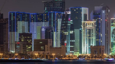 Téléchargez les photos : Doha gratte-ciel dans l'horizon du centre-ville timelapse nocturne, Qatar, Moyen-Orient Tours éclairées sur une baie ouest reflétées dans une eau du Golfe. - en image libre de droit