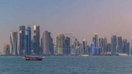 Téléchargez les photos : Doha skyline centre-ville jour à nuit transition timelapse, Qatar, Moyen-Orient. Des gratte-ciel éclairés sur une baie ouest reflétés dans une eau du Golfe - en image libre de droit