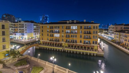 Photo for Canal with bridge aerial top view in Venice-like Qanat Quartier of the Pearl precinct of Doha night timelapse, Qatar. Evening illumination reflected in water - Royalty Free Image