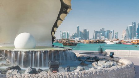 Foto de Corniche con fuente con una ostra con una perla gigantesca dentro de timelapse con el horizonte de Doha y barcos detrás de ella. Gente caminando - Imagen libre de derechos