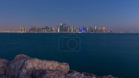 Téléchargez les photos : Skyline de la ville arabique de Doha la nuit au jour timelapse de transition au Qatar, capturé dans la matinée très tôt avant le lever du soleil avec des gratte-ciel éclairés. Vue de Corniche Promenade - en image libre de droit