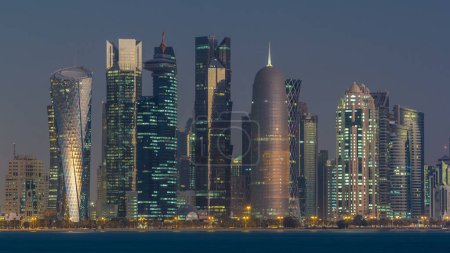 Foto de Skyline de la ciudad árabe de Doha noche a día timelapse transición en Qatar, capturado en la madrugada antes del amanecer con rascacielos iluminados. Vista desde Corniche Promenade - Imagen libre de derechos