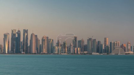Foto de Skyline de la ciudad árabe de Doha timelapse en Qatar, capturado en la madrugada durante el amanecer con los ricos colores cálidos del sol reflejándose en los rascacielos de cristal. - Imagen libre de derechos