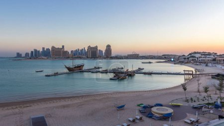 Foto de Vista desde Katara Beach día a noche timelapse transición después del atardecer en Doha, Qatar, hacia la Bahía Oeste y el centro de la ciudad. Rascacielos iluminados. Antiguo barco en primer plano - Imagen libre de derechos