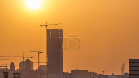 Photo for A tower in Doha timelapse, Qatar, under construction, silhouetted against the sunset. Close up view with many cranes - Royalty Free Image