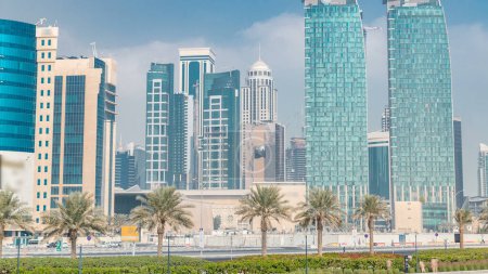 Photo for The skyline of Doha seen from Park timelapse, Qatar. Trees and palms on foreground. Modern skyscrapers and towers on background. Traffic on road - Royalty Free Image