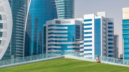 Foto de El distrito de gran altura de Doha timelapse, visto desde el Hotel Park, con césped verde y colina artificial en primer plano. Rascacielos y palmeras - Imagen libre de derechos