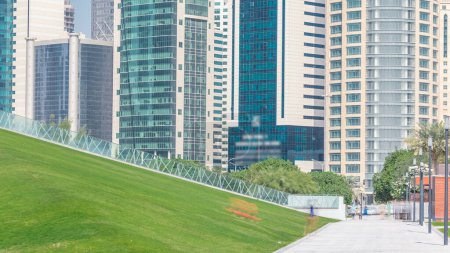 Téléchargez les photos : Le quartier de grande hauteur de Doha timelapse, vu de l'Hôtel Park, avec pelouse verte et colline artificielle au premier plan. Gratte-ciels et palmiers - en image libre de droit