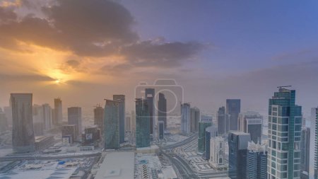 Photo for Skyscrapers at sunset timelapse in the skyline of commercial center of Doha, the capital Qatar. Aerial top view at foggy weather. Cloudy orange sky - Royalty Free Image
