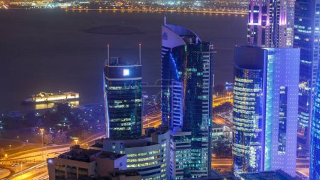 Téléchargez les photos : L'horizon de la région de West Bay depuis le sommet à Doha timelapse, Qatar. Éclairage moderne gratte-ciel vue aérienne depuis le toit la nuit. Golfe en arrière-plan et circulation sur la route - en image libre de droit
