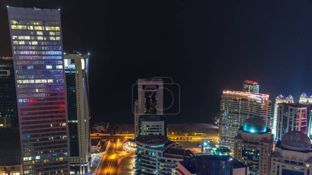 Photo for The skyline of the West Bay area from top in Doha timelapse, Qatar. Illuminated modern skyscrapers aerial view from rooftop at night. Gulf on background and traffic on the road - Royalty Free Image