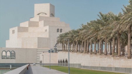 Foto de Museo de Arte Islámico de Qatar timelapse en su isla artificial junto a Doha Corniche, con dhows amarrado en la bahía que lo rodea. Vista frontal con palmeras - Imagen libre de derechos