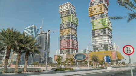 Foto de Doha horizonte timelapse con colorido edificio Al Marina Twin Towers situado en la zona de Lusail de la capital de Qatar. Palmeras y árboles. Tráfico en la carretera - Imagen libre de derechos