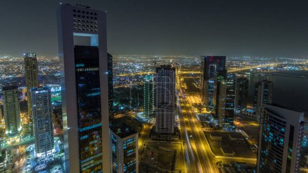 Photo for The skyline of the West Bay area from top in Doha timelapse, Qatar. Illuminated modern skyscrapers aerial view from rooftop at night. Traffic on the road - Royalty Free Image