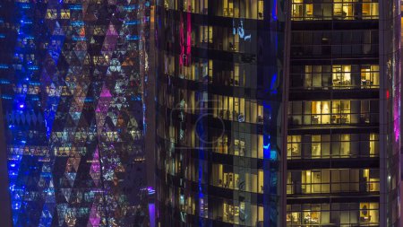 Foto de Ventanas timelapse del edificio de varios pisos de vidrio y acero de iluminación de oficinas y los trabajadores dentro. Iluminación nocturna de rascacielos. Doha, Qatar - Imagen libre de derechos