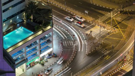 Téléchargez les photos : Trafic à l'intersection avec le tram la nuit timelapse aérienne du haut, avec piscine et parking à l'intérieur du bâtiment, Dubai Marina - en image libre de droit