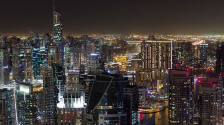Foto de Dubai Marina con yates nocturnos timelapse aéreo. Luces brillantes y rascacielos más altos a lo largo del canal durante una noche clara. Panorámica desde arriba - Imagen libre de derechos