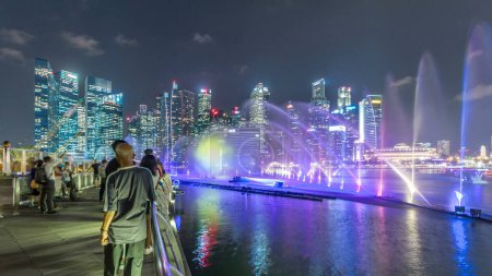 Photo for Light and Water Show along promenade in Marina Bay timelapse. The show of dancing fountains is one of biggest attractions in Singapore by night. Illuminated skyscrapers on background - Royalty Free Image