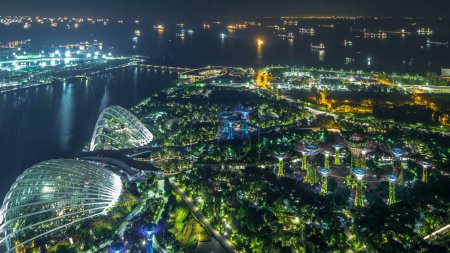 Foto de Vista aérea de Gardens by the Bay y barcos industriales en Singapur timelapse puerto. Iluminación nocturna del puerto - Imagen libre de derechos