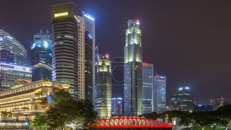Téléchargez les photos : Singapore business district skyscrapers in the night time with water reflections timelapse hyperlapse. Bridge over a river. Illuminated towers with blinking lights in windows - en image libre de droit