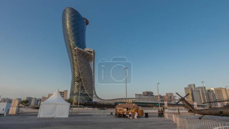 Photo for Abu Dhabi, UAE - Feb 25, 2023: National Exhibition Centre (ADNEC) where IDEX Military Exhibition was held day to night transition timelapse hyperlapse. View with modern skyscraper behind helicopters - Royalty Free Image