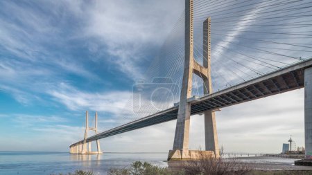 Vasco da Gama bridge timelapse hyperlapse with reflection on water and blue cloudy sky. Cable-stayed bridge and Tagus river. Lisbon, Portugal.