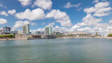 Panorama showing Parque das Nacoes or Park of Nations district timelapse in Lisbon, Portugal. Telecabine cable cars overlook Vasco da Gama bridge on Tagus river. Modern buildings reflected in water