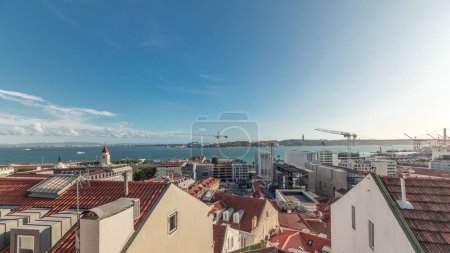 Panorama showing red roofs timelapse and 25 de Abril Bridge, Iconic suspension bridge over Tagus River in Lisbon, Portugal. Aerial view from Miradouro de Santa Catarina. Classic Viewpoint at sunny day