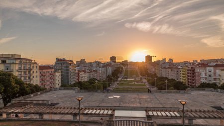 Panorama showing sunset over lawn at Alameda Dom Afonso Henriques with colorful buildings and the Luminous Fountain aerial timelapse. View from above with evening sky in Lisbon, Portugal