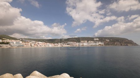 Téléchargez les photos : Panorama avec vue sur la ville de Sesimbra et Port Timelapse, Portugal. Paysage Skyline avec bateaux, maisons et plage depuis le phare sur une jetée. Resort dans le quartier de Setubal. De beaux nuages - en image libre de droit