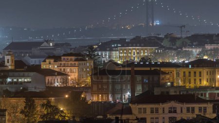 Aerial view towards Barrio Alto and 25th of April Bridge night timelapse, Lisbon, Portugal. Colorful historic buildings with evening illumination
