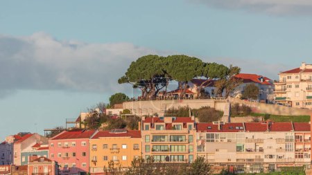 Téléchargez les photos : Point de vue célèbre Miradouro da Senhora do Monte avec vue sur la ville de Lisbonne timelapse pendant le coucher du soleil avec des maisons colorées autour, Lisbonne, Portugal. Nuages sur le ciel au-dessus des arbres verts - en image libre de droit