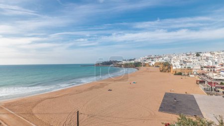 Téléchargez les photos : Panorama montrant une large plage de sable fin et l'océan Atlantique dans la ville d'Albufeira timelapse. Des maisons blanches au sommet des falaises. Vue aérienne d'en haut. Nuages sur un ciel bleu. Algarve, Portugal - en image libre de droit