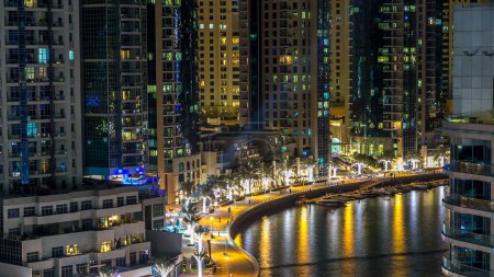 Téléchargez les photos : Promenade à Dubai Marina timelapse la nuit, Émirats arabes unis. Vue de dessus avec palmiers et tours sur le front de mer. Dubai Marina est un quartier de Dubaï avec canal artificiel - en image libre de droit