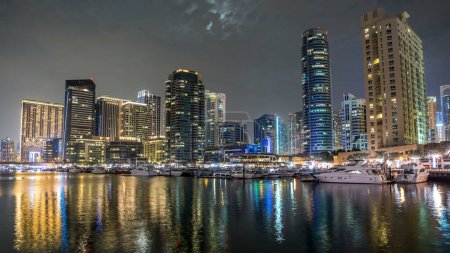 Photo for Dubai Marina towers with floating yachts and boats timelapse hyperlapse, United Arab Emirates. District in Dubai with an artificial canal. Full moon in the cloudy sky - Royalty Free Image