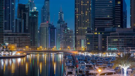 Foto de Dubai Marina waterfront with towers and yachts from bridge in Dubai night to day transition timelapse, Emiratos Árabes Unidos. Distrito con canal artificial y rascacielos iluminados antes del amanecer - Imagen libre de derechos