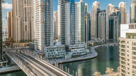 Photo for Dubai Marina at evening timelapse with trails of boats on the water and cars traffic on bridge road, Dubai, UAE. Aerial view from rooftop with shadows movement - Royalty Free Image