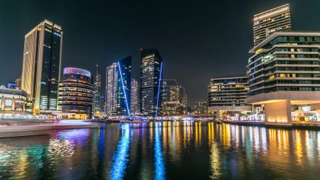 Foto de Paseo marítimo de Dubai Marina con yates y modernas torres reflejadas en el agua desde el paseo marítimo en Dubai night timelapse, Emiratos Árabes Unidos. - Imagen libre de derechos