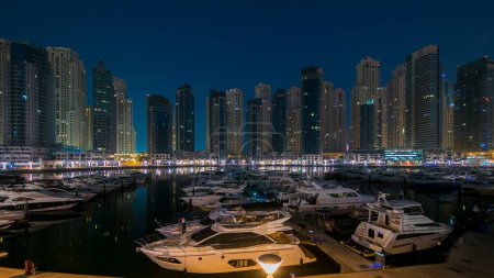 Photo for Dubai Marina at blue hour night to day transition timelapse with many yachts from yacht club, Glittering lights and tallest skyscrapers during a clear morning with blue sky. Lights turn off - Royalty Free Image