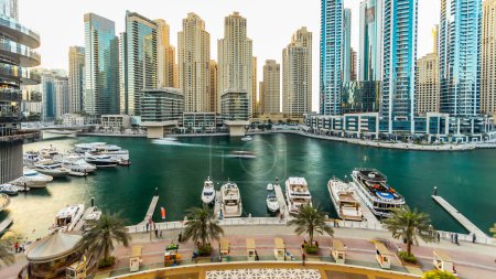 Photo for Dubai marina with modern buildings and traditional boat timelapse. Top aerial view of modern towers at sunset time from above - Royalty Free Image