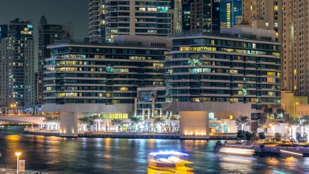 Téléchargez les photos : Promenade à Dubai Marina timelapse la nuit, Émirats arabes unis. Vue depuis le pont avec palmiers, bateaux flottants et tours modernes. Quartier avec canal artificiel - en image libre de droit