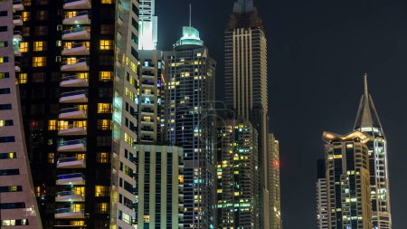 Foto de Noche vista de cerca desde el paseo marítimo en Dubai Marina modernas torres con luces parpadeantes timelapse hyperlapse, Emiratos Árabes Unidos. Rascacielos iluminados - Imagen libre de derechos