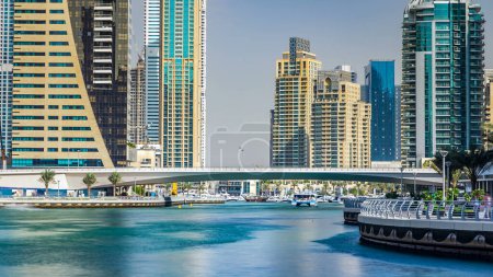 Foto de Dubai Marina modernas torres y puente con yates flotantes y barcos del paseo marítimo timelapse, Emiratos Árabes Unidos. Los rascacielos más altos. Cielo azul - Imagen libre de derechos